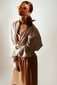 Trendy woman posing in oversized shirt and sunglasses, exuding modern fashion style.