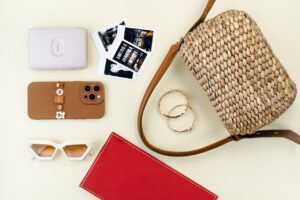 Flat lay of chic accessories including a wicker bag, phone, glasses, and jewelry for a stylish look.