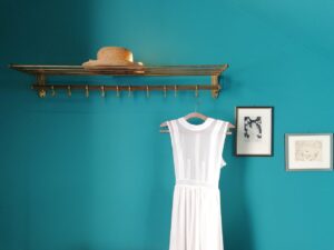 Minimalist interior featuring a white dress and straw hat against a teal wall with framed art.