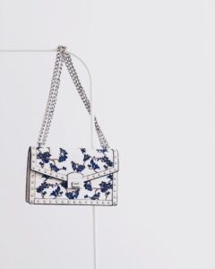 Elegant white handbag with blue floral design and silver chain, perfect for fashion enthusiasts.